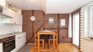 A compact kitchen with white cabinets, a wooden dining table with chairs, a clock, and a framed picture on the brick wall. - Centrally located apartment for 4 people and dog (Greetsiel)