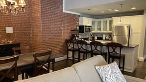 Una cocina moderna con armarios blancos, un refrigerador de acero inoxidable y un comedor con sillas y mesa de madera.