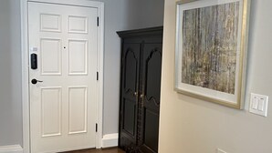 Un pasillo con una puerta blanca, un armario de madera oscura, un cuadro abstracto enmarcado y una rejilla en la pared.