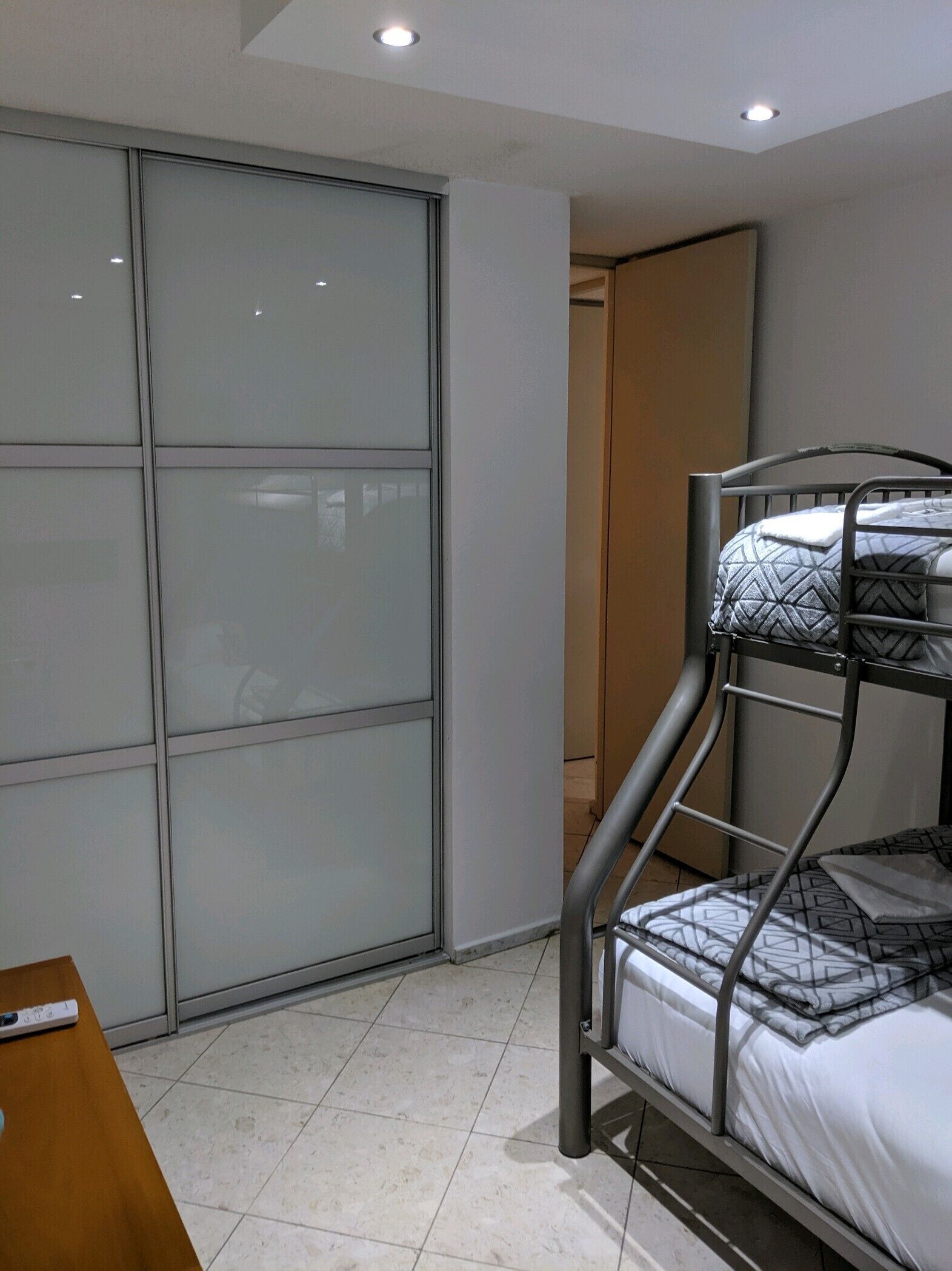 A bunk bed with patterned bedding, a sliding glass door, and a wooden desk with a remote control.