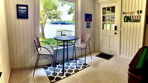 A room with a window view of a lake, a round table with chairs, a door with a sign, and a small rug.