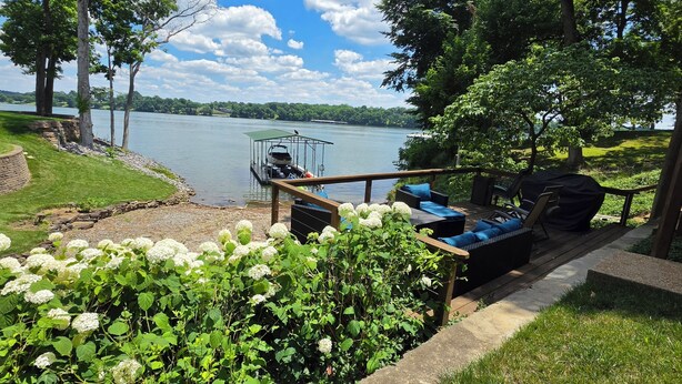 A lakeside deck with a boat dock, outdoor seating, and a stone wall.