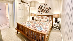 A bedroom with a wooden bed, patterned bedding, a wall art piece, and two bedside lamps.