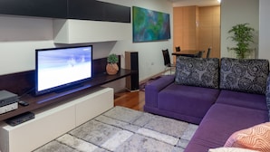 A modern living room with a flat-screen TV, a sofa, a coffee table, and a dining area with a table and chairs. - Porto H Dragão (Porto)