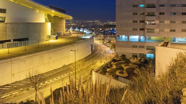 A modern building with a curved facade, a parking area, and a view of a distant cityscape at night. - Porto H Dragão (Porto)