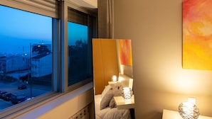 A hotel room with a large window, a bed with pillows, a bedside table with a lamp, and a painting on the wall. - Porto H Dragão (Porto)