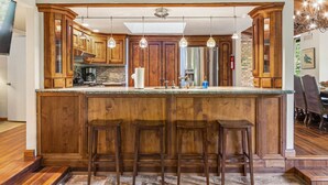 Une cuisine avec des meubles en bois, un plan de travail en marbre et trois tabourets de bar.