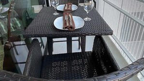 A balcony with a table set for two, wicker chairs, and a glass railing. - ILLUME/Modern New Condo/ Pool & Downtown Views/Gym (Nashville)