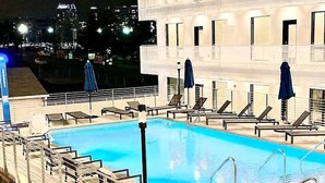 A swimming pool with sun loungers and umbrellas, surrounded by a building with multiple balconies. - ILLUME/Modern New Condo/ Pool & Downtown Views/Gym (Nashville)