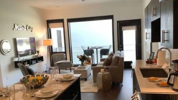 A modern living room with a dining area, a kitchen, and a balcony. - ILLUME/Modern New Condo/ Pool & Downtown Views/Gym (Nashville)