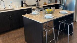 A modern kitchen with dark cabinetry, a stainless steel refrigerator, and a central island with stools. - ILLUME/Modern New Condo/ Pool & Downtown Views/Gym (Nashville)