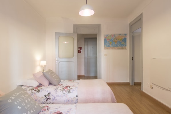 Une chambre à coucher avec un lit, une table de chevet, une lampe, une carte accrochée au mur et une porte donnant sur une autre pièce.