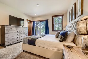 Quarto com uma cama grande, cômoda, televisão e janela com cortinas.