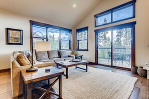 A spacious living room with a sofa, coffee table, and large windows offering views of the outdoors.