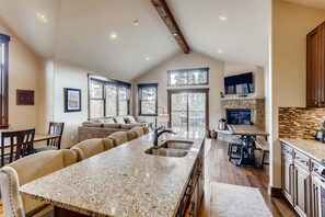 A spacious kitchen with a granite countertop, a stone fireplace, and large windows.