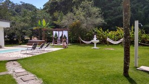 Un jardin avec une piscine, des chaises longues, un gazebo et un hamac.