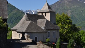 A traditional stone building with a steep roof, a bell tower, and a mountain backdrop.