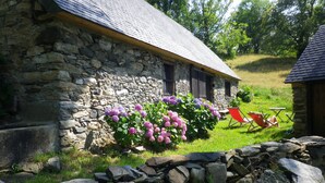 A stone building with a sloped roof, a garden with purple flowers, and a red chair outside.