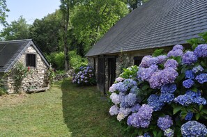 A stone cottage with a sloped roof, surrounded by lush greenery and hydrangea flowers. - SHEEPFOLD PANORAMIC VIEW ON THE VALLEY OF ARGELES AND MOUNTAINS (ARTALENS -SOUIN)