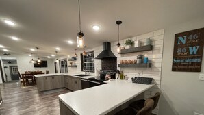 A modern kitchen with a central island, pendant lighting, and a backsplash with copper cookware. - Superior Adventures — Luxury 80-Acre Executive Retreat (Shingleton)