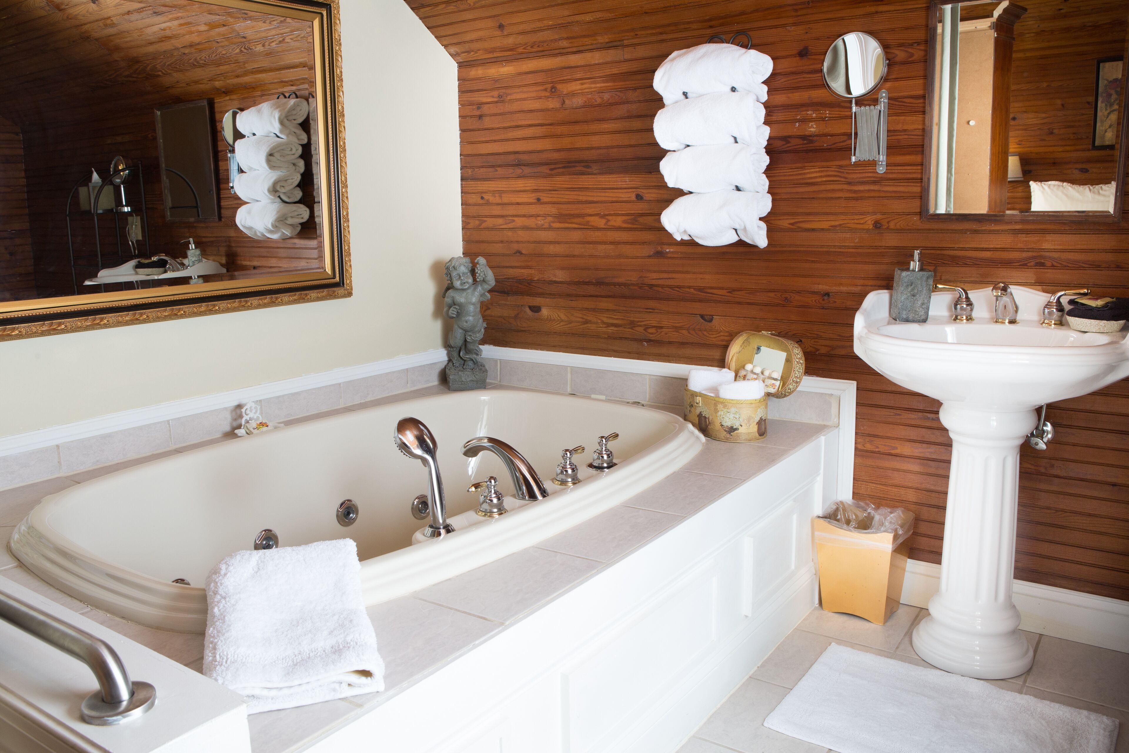 A bathroom with a large bathtub, a pedestal sink, and wooden paneling on the walls.