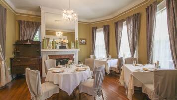 A dining room with multiple tables set for a meal, a fireplace, and a chandelier.