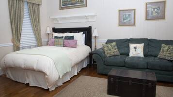 A bedroom with a bed, a green sofa, a dark chest of drawers, and two framed pictures on the wall.