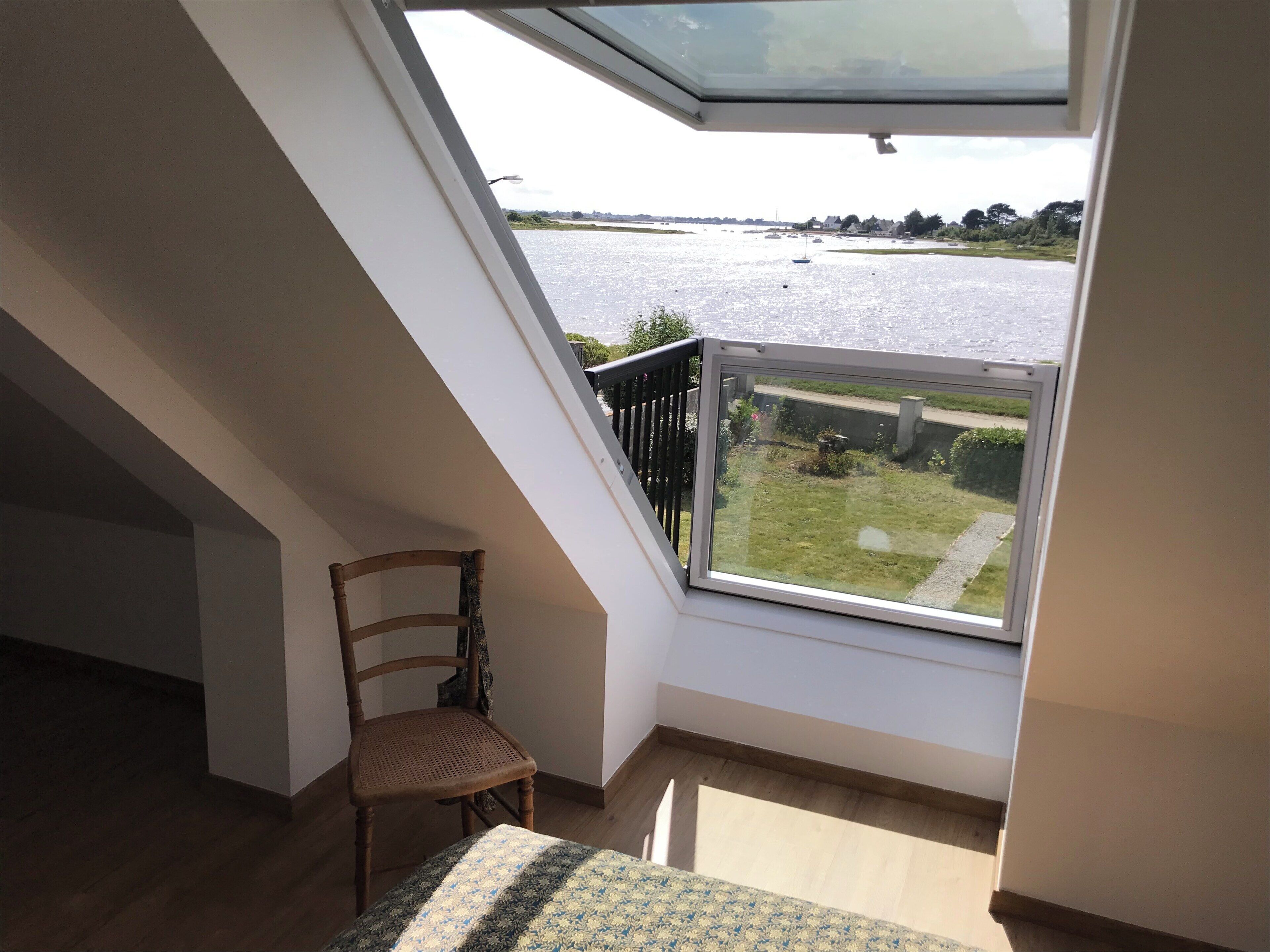 A room with a skylight overlooking a body of water, a wooden chair, and a patterned rug.