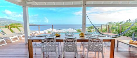 A wooden deck with a table set for dining, overlooking a scenic ocean view.