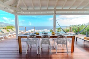 A wooden deck with a table set for dining, overlooking a scenic ocean view.