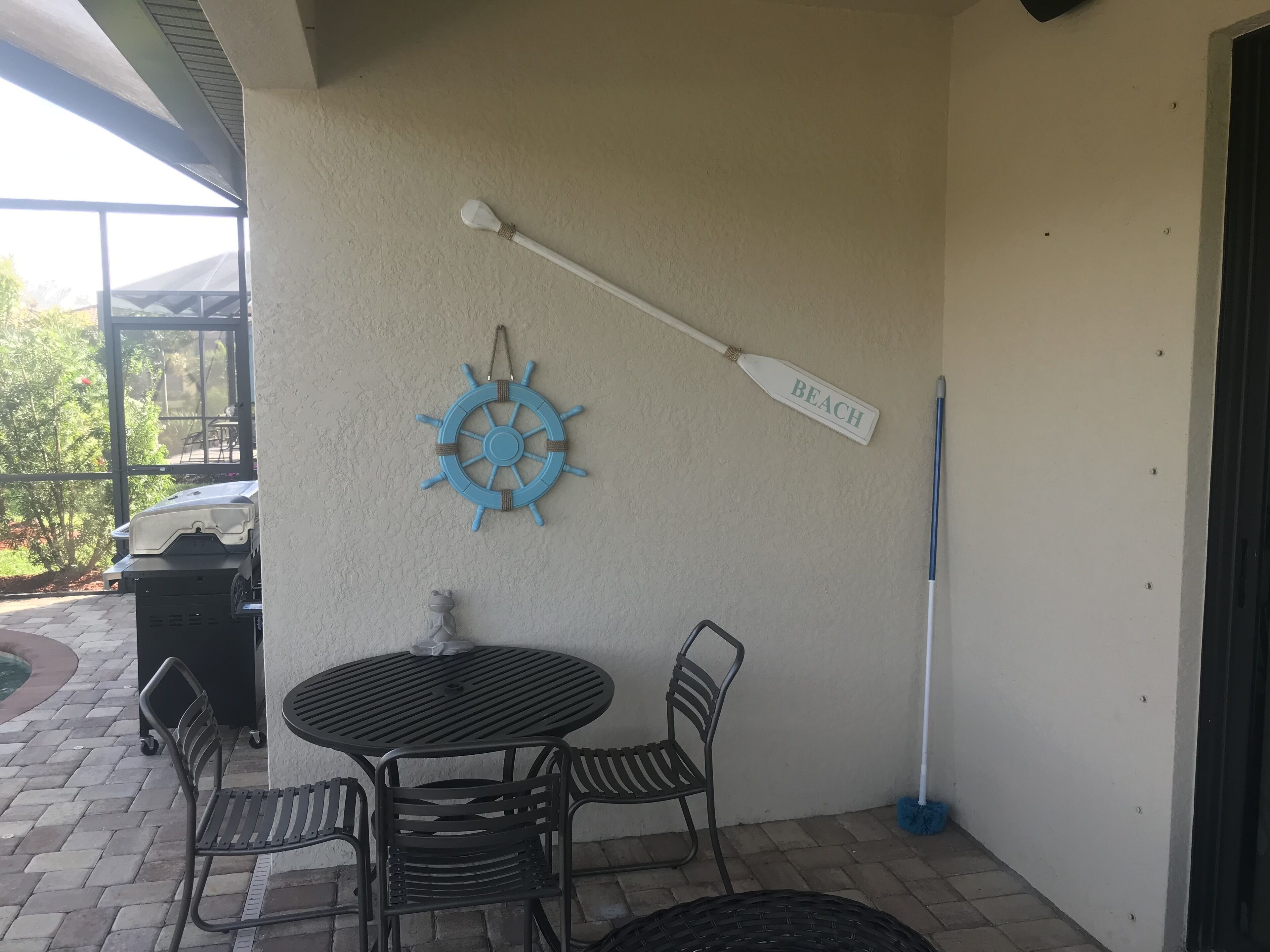 A patio area with a round table and chairs, a life preserver decoration, a paddle labeled "BEACH", and a mop leaning against the wall.