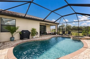 Ein Schwimmbecken mit überdachter Terrasse, Grill und Topfpflanzen.