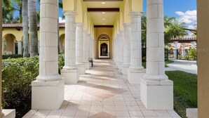 A corridor with white columns, a tiled floor, and a view of a building in the distance. - PARADISE MEETS PRIVACY WITH AMAZING WATER VIEW & HEATED POOL (Venice)