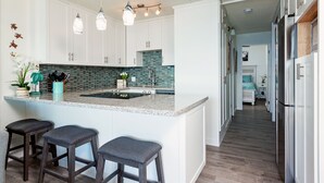 A modern kitchen with white cabinets, a large island with bar stools, and a backsplash with blue tiles. - Endless Waves, Incredible Direct Oceanfront Views! (Wailuku)