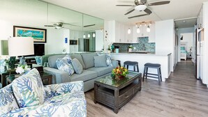 A modern living room with a sofa, coffee table, and a kitchen area with a bar. - Endless Waves, Incredible Direct Oceanfront Views! (Wailuku)
