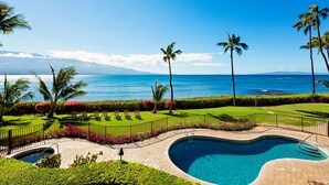 A pool area with a curved design, surrounded by a well-manicured lawn and palm trees, overlooking a clear blue ocean and distant mountains. - Endless Waves, Incredible Direct Oceanfront Views! (Wailuku)