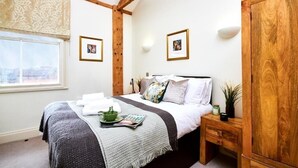 Een slaapkamer met een bed, nachtkastje, houten kledingkast, een raam met uitzicht en twee ingelijste foto's aan de muur.
