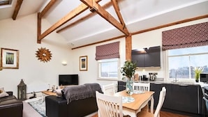 Een gezellige woonkamer met een bank, een eettafel met stoelen, een televisie en een keuken met een raam.