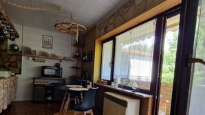 Une cuisine rustique avec un coin repas, des murs en pierre et une vue dégagée sur l’extérieur grâce à une grande fenêtre.