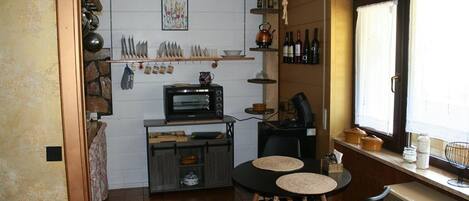 Cuina compacta amb forn integrat, taula petita amb seients i finestra amb cortines.