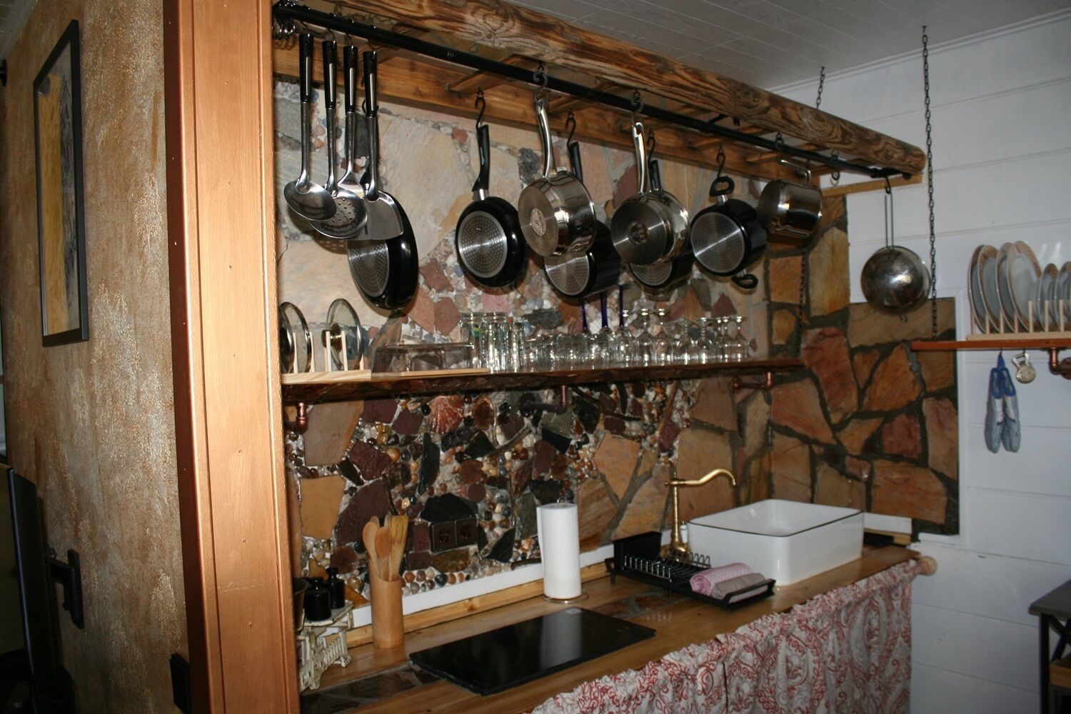 Une cuisine avec un mur recouvert de pierres apparentes, des ustensiles de cuisine suspendus et un plan de travail en bois.