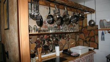 Une cuisine avec un mur recouvert de pierres apparentes, des ustensiles de cuisine suspendus et un plan de travail en bois.