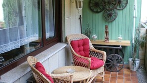 Une terrasse avec des chaises en osier, une table et un mur végétal agrémenté de roues décoratives.
