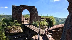 Un antiguo arco de piedra con un pasillo de madera que lo atraviesa, rodeado de follaje y colinas.