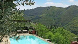 Una piscina rectangular con cubierta de madera, rodeada de vegetación exuberante y vistas a un paisaje montañoso.