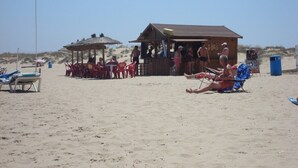Eine Strandansicht mit einer Holzhütte, Liegestühlen und einem Gebäude mit Strohdach.