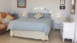 Ein Schlafzimmer mit einem Bett, zwei Nachttischen, einer Kommode und einem Spiegel. An der Wand hängt ein Gemälde.