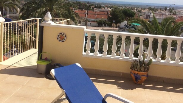 Ein Balkon mit blauem Liegestuhl, einem Topfpflanzen und Blick auf Stadt und Meer.