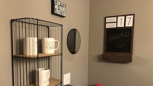 A shelf with mugs, a coffee maker, and a calendar on the wall.