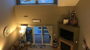A high-ceilinged living room with a large window, a fireplace, and a television.